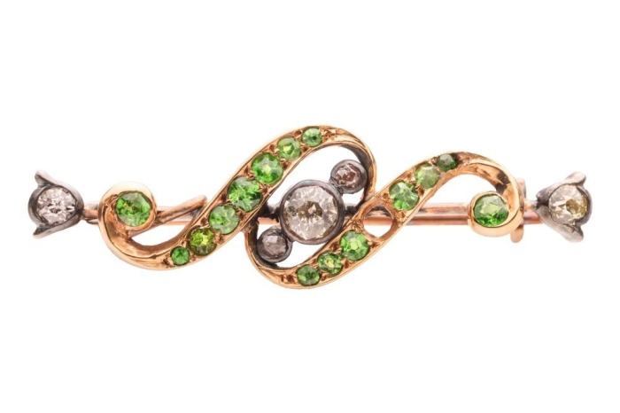 An Edwardian demantoid garnet and diamond bar brooch; centred with collet-set old-cut diamonds, between a bypassing scrollwork mount set with graduated circular-cut demantoid garnets, brooch fittings to the back, unmarked yellow metal testing as 14ct, 3.4