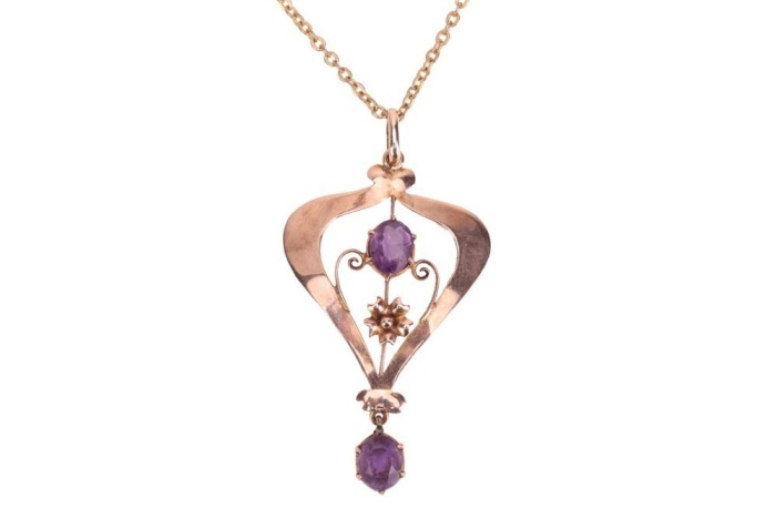 An Edwardian amethyst-set pendant, claw-set with two oval-cut amethysts, in a yellow metal mount of scrolling and floral design, marked &lsquo;9ct&rsquo;, to a base metal chain; total weighable: 1.4 grams