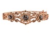 A hinged bracelet set with black star sapphires; the openwork scrolled mount with twisted rope border and beaded accents, set with three graduated oval black star sapphire cabochons, fastens with a tongue clasp with push-in thumbpiece, in yellow metal sta