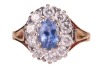 A sapphire and diamond cluster ring in 18ct, centred with an oval-cut sapphire of 6.7 x 4.6 x 3.2mm, encompassed by ten round brilliant-cut diamonds with an estimated total weight of 0.57ct, between foliate shoulders, ring head 1.3 x 1.1 cm, size L, 3.8 g - 2