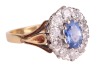 A sapphire and diamond cluster ring in 18ct, centred with an oval-cut sapphire of 6.7 x 4.6 x 3.2mm, encompassed by ten round brilliant-cut diamonds with an estimated total weight of 0.57ct, between foliate shoulders, ring head 1.3 x 1.1 cm, size L, 3.8 g - 4