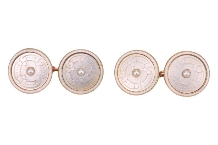 A pair of mother-of-pearl cufflinks, of circular form, each set with an engraved mother-of-pearl panel, centred with a split pearl accent, within a white enamelled frame, in yellow metal surface testing as 14ct, panel measures 1.3 cm across, 4.1 grams. Pl