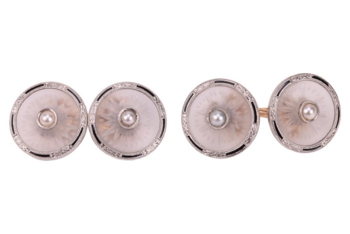 Krementz - a pair of rock crystal and split pearl cufflinks; the round and frosted rock crystal panels with carved radiating patterns, in a millgrained frame with foliate and black enamel details, centred with an applied split pearl, bar link connections 