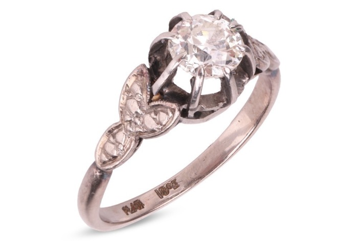 A late Art Deco diamond solitaire ring, centred with an Old-European cut diamond of 5.6 mm, estimated weight 0.70ct, in a buttercup mount between foliate shoulders, white metal stamped '18ct PLAT', size M&frac12;, 3.4 grams. Diamond approximately measures 5.6 x 
