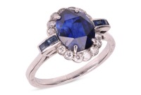 A sapphire and diamond cluster ring; the oval mixed-cut sapphire claw mounted within a border of fourteen round brilliant cut diamonds, with two calibr&eacute; cut sapphires to each shoulder. Plain D-shaped shank, unmarked, shank surface testing as 14ct and moun