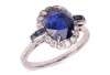 A sapphire and diamond cluster ring; the oval mixed-cut sapphire claw mounted within a border of fourteen round brilliant cut diamonds, with two calibr&eacute; cut sapphires to each shoulder. Plain D-shaped shank, unmarked, shank surface testing as 14ct and moun