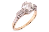 A diamond solitaire ring, the central diamond measuring approximately 7.5mm, with an estimated carat weight of 1.70ct, flanked by two bezel-set baguette-cut diamonds, in a bi-colour metal mount marked &lsquo;18ct&rsquo;, size L; 3.8 grams.