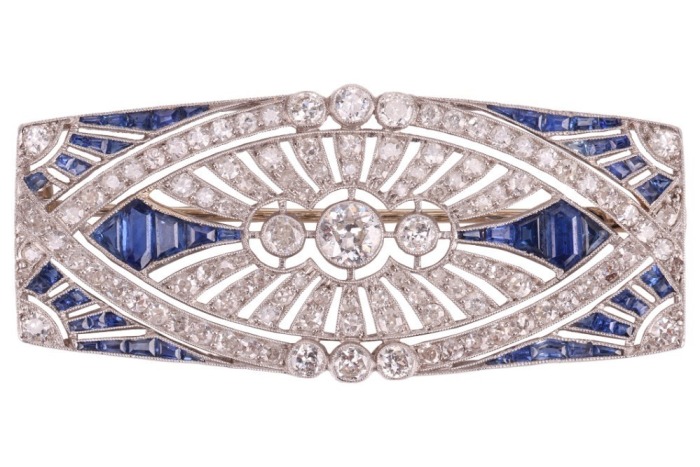 An Art Deco sapphire and diamond-set brooch, of architectural design; the rounded rectangular openwork frame centrally-set with three old-cut diamonds, with millegrain bezel surround, the largest diamond measuring approximately 4.5mm, within a navette-sha