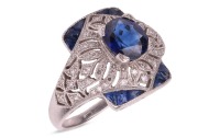 A sapphire and diamond panel ring, centred with an oval-cut sapphire of 6.8 x 6.2 x 3.8mm, in a millgrained pierced mount encrusted with single-cut diamonds with calibre-cut sapphire corners, white metal surface testing as platinum, ring head 1.5 x 1.2 cm