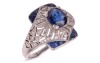 A sapphire and diamond panel ring, centred with an oval-cut sapphire of 6.8 x 6.2 x 3.8mm, in a millgrained pierced mount encrusted with single-cut diamonds with calibre-cut sapphire corners, white metal surface testing as platinum, ring head 1.5 x 1.2 cm