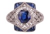 A sapphire and diamond panel ring, centred with an oval-cut sapphire of 6.8 x 6.2 x 3.8mm, in a millgrained pierced mount encrusted with single-cut diamonds with calibre-cut sapphire corners, white metal surface testing as platinum, ring head 1.5 x 1.2 cm - 2