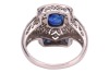 A sapphire and diamond panel ring, centred with an oval-cut sapphire of 6.8 x 6.2 x 3.8mm, in a millgrained pierced mount encrusted with single-cut diamonds with calibre-cut sapphire corners, white metal surface testing as platinum, ring head 1.5 x 1.2 cm - 3