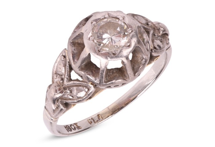 A diamond-set solitaire ring, composed of an illusion-set round brilliant cut diamond, measuring approximately 4.5mm, with an estimated carat weight of 0.36ct, the high gallery leading to foliate-style shoulders, to a white metal shank marked &lsquo;18ct&rsquo;, size