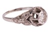 A diamond-set solitaire ring, composed of an illusion-set round brilliant cut diamond, measuring approximately 4.5mm, with an estimated carat weight of 0.36ct, the high gallery leading to foliate-style shoulders, to a white metal shank marked &lsquo;18ct&rsquo;, size - 4