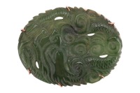 A mottled dark green nephrite jade panel brooch, the oval plaque carved with a sinuous dragon in cloud scrolls, in a plain 9ct yellow gold brooch frame, hallmarked for London 1975, 45mm x 33mm, 13.3g gross.