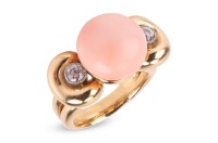 An angelskin coral and diamond dress ring, centred with a button-shaped corallium secundum of 12.6 mm, between bow shoulders adorned with two old-cut diamonds in millgrained collets, with an estimated total weight of 0.28ct, yellow metal stamped '18K', si