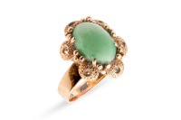 A jadeite ring, the oval jadeite cabochon centrally set in a four-prong setting, with textured surround featuring bead detailing, to a flat-shaped shank in yellow metal marked &lsquo;14K&rsquo;, size P; 5.7 grams