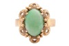 A jadeite ring, the oval jadeite cabochon centrally set in a four-prong setting, with textured surround featuring bead detailing, to a flat-shaped shank in yellow metal marked &lsquo;14K&rsquo;, size P; 5.7 grams - 2