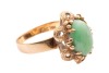 A jadeite ring, the oval jadeite cabochon centrally set in a four-prong setting, with textured surround featuring bead detailing, to a flat-shaped shank in yellow metal marked &lsquo;14K&rsquo;, size P; 5.7 grams - 3