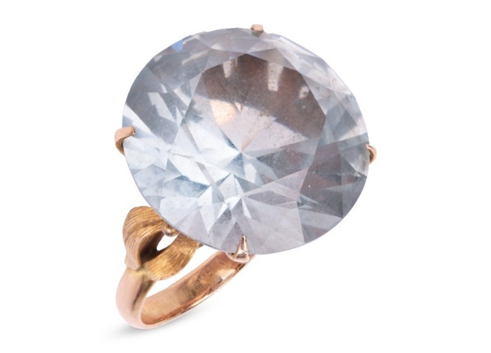 A large synthetic spinel dress ring; set with a round synthetic spinel in pale blue, claw set to a yellow metal mount with floral motif shoulders, to a tapered D-profile shank, marked as '14k', ring head measures 1.9 cm across, ring size M&frac12;, total weight 