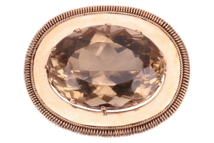 A large smoky quartz pendant cum brooch, containing a large oval-cut smoky quartz of 3.5 x 2.5 cm, claw-set to an oval surround with coiled edge, hinged bail and brooch fittings to the reverse, unmarked pinkish-yellow metal surface testing as 14ct, 5.0 cm