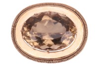A large smoky quartz pendant cum brooch, containing a large oval-cut smoky quartz of 3.5 x 2.5 cm, claw-set to an oval surround with coiled edge, hinged bail and brooch fittings to the reverse, unmarked pinkish-yellow metal surface testing as 14ct, 5.0 cm