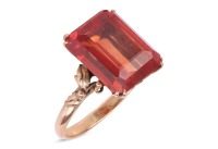 A synthetic orange sapphire ring, with an emerald-cut synthetic sapphire in reddish-orange colour, double claw set on a yellow metal mount, floral details on gallery and shoulders, to a D-profile shank, marked '14k', ring size O, total weight of item 4.8 