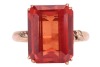 A synthetic orange sapphire ring, with an emerald-cut synthetic sapphire in reddish-orange colour, double claw set on a yellow metal mount, floral details on gallery and shoulders, to a D-profile shank, marked '14k', ring size O, total weight of item 4.8 - 2
