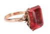 A synthetic orange sapphire ring, with an emerald-cut synthetic sapphire in reddish-orange colour, double claw set on a yellow metal mount, floral details on gallery and shoulders, to a D-profile shank, marked '14k', ring size O, total weight of item 4.8 - 3