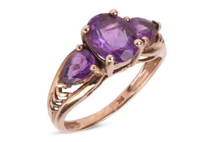 An amethyst trilogy ring, centred with an oval-cut amethyst flanked by further two pear-cut amethysts, with pierced chevron shoulders to tapering shank, in yellow metal stamped '9K', size K, 2.1 grams.
