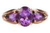 An amethyst trilogy ring, centred with an oval-cut amethyst flanked by further two pear-cut amethysts, with pierced chevron shoulders to tapering shank, in yellow metal stamped '9K', size K, 2.1 grams. - 2