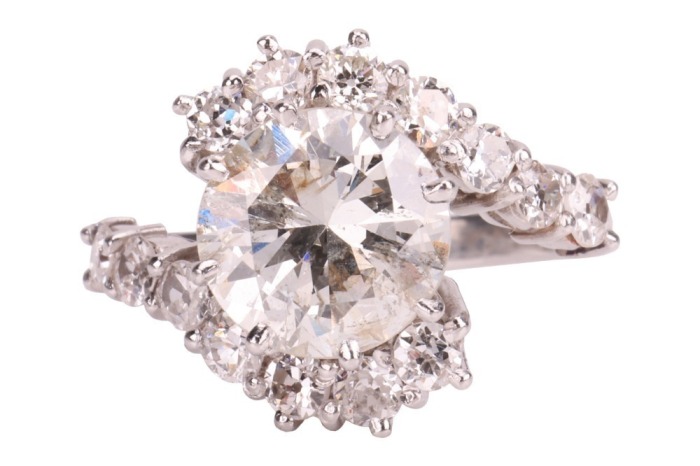 A diamond-set crossover-style ring, featuring a central round brilliant diamond, measuring approximately 9.1mm x 5.2mm, with an estimated carat weight of 3.00ct and an estimated colour and clarity grade of J/K and I2, the crossover-style shoulders each cl