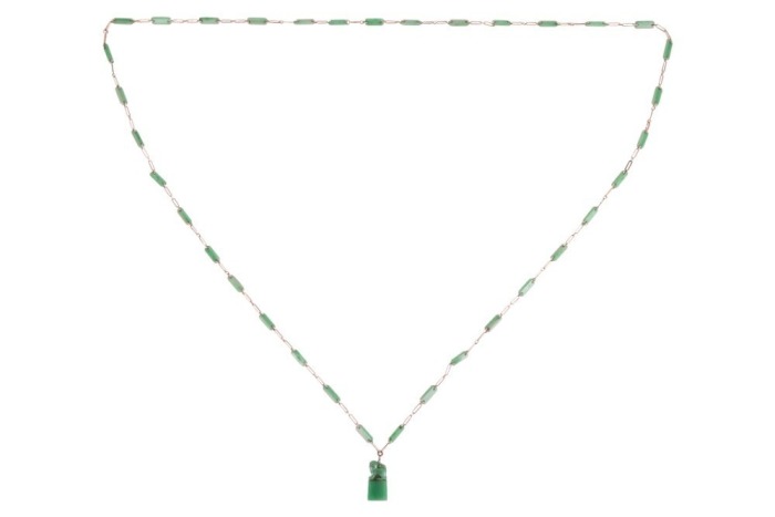A long jadeite link chain, comprising a series of Figaro links, flanked by faceted jadeite bar links with a chamfered edge, suspending a carved jadeite Fuu dog seal with vacant panel, yellow metal surface testing as 14ct, with a gilt suspension loop bail,