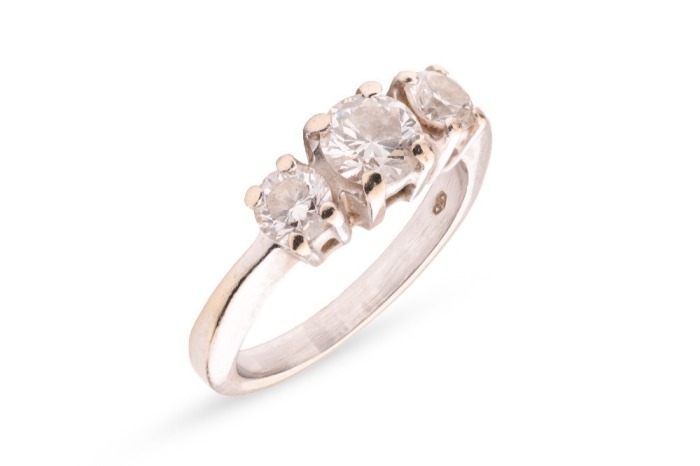 A diamond trilogy ring, with an estimated total diamond weight of 1.00ct, comprising three graduated round brilliant-cut diamonds in claw setting, between tapered shoulders leading to a flat shank, white metal stamped '750', size J, 4.3 grams. Approximate
