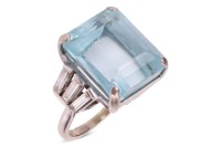 An Art Deco style aquamarine and diamond-set ring, claw-set with a step-cut aquamarine, measuring approximately 15.8mm x 13.5mm, flanked by six baguette-cut diamonds, in a tapering design, to an unmarked white metal shank surface tested as 18ct; 10.0 gram