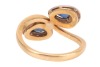 A sapphire and diamond crossover ring, consisting of two pear-shaped sapphires claw-set on white metal mounts, each encircled with diamond accents, to a tapered flat shank in yellow metal, marked as '750', ring size M&frac12;, total weight of item 4.6 grams. - 4