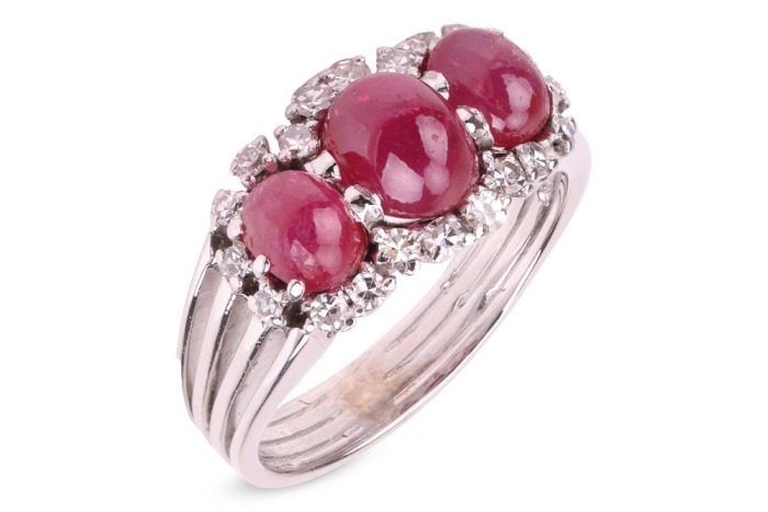 A ruby cabochon and diamond dress ring, comprising three graduated oval ruby cabochons, embellished with single-cut diamonds, to a shank composed of four knife-edged bands, in white metal stamped '750', size R&frac12;, 7.5 grams.