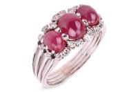 A ruby cabochon and diamond dress ring, comprising three graduated oval ruby cabochons, embellished with single-cut diamonds, to a shank composed of four knife-edged bands, in white metal stamped '750', size R&frac12;, 7.5 grams.