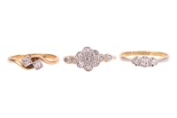Three rings; comprising a diamond-set floral cluster ring, in a bi-colour metal mount marked &lsquo;18ct&rsquo;, size O1/2, a diamond-set three-stone ring, in a bi-colour metal mount marked &lsquo;18ct&rsquo;, size N, and a diamond-set crossover ring in a yellow metal mount mark