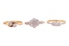 Three rings; comprising a diamond-set floral cluster ring, in a bi-colour metal mount marked &lsquo;18ct&rsquo;, size O1/2, a diamond-set three-stone ring, in a bi-colour metal mount marked &lsquo;18ct&rsquo;, size N, and a diamond-set crossover ring in a yellow metal mount mark