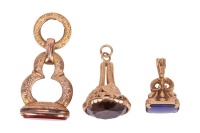 A 9 carat gold and smoky quartz seal, decorated with shields; together with a further seal set with a dyed blue chalcedony, and a 19th century gilt metal seal with carnelian. (3)