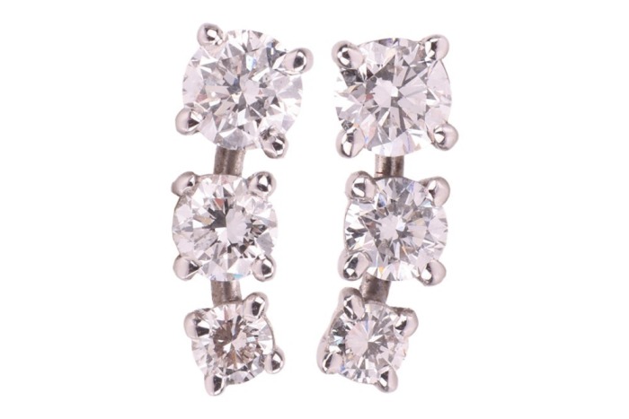 A pair of diamond-set stud earrings, each consisting of three graduated round brilliant-cut diamonds, with an estimated total weight of 1.00ct for the pair, ear post fittings, butterfly backs deficient, unmarked white metal surface testing as 18ct, 1.3 cm