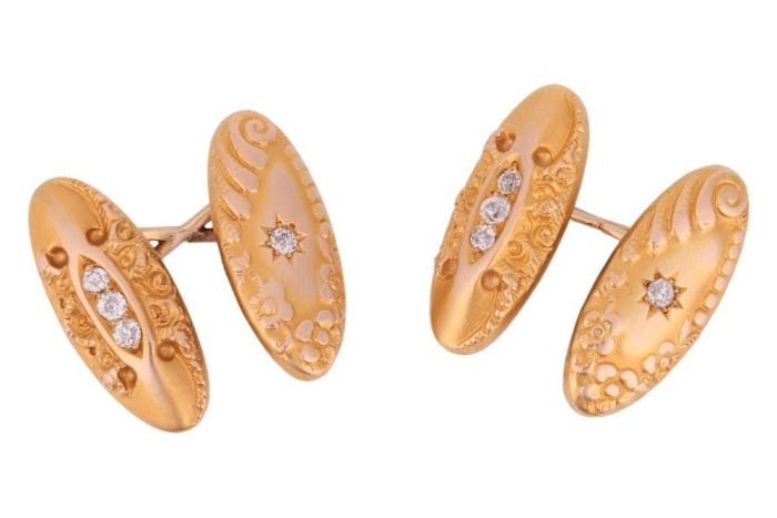 A pair of diamond-set cufflinks, of elongated oval form with repousse design, one panel centred with a star-set old-cut diamond, the other pave-set with a row of three old-cut diamonds in a navette mount, connected by a figure of eight link, unmarked yell