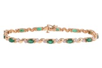 An emerald and diamond line bracelet, comprising thirteen oval-cut emeralds in claw mounts, flanked by hinged links in the form of a tilde, with single-cut diamond accents in illusion settings, tongue clasp fastening, yellow metal marked '14K', 18.7 cm lo