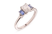 A diamond and sapphire trilogy ring, featuring a central claw-set emerald-cut diamond of 0.91ct, E colour and VVS2 clarity, the diamond flanked each side by a claw-set emerald-cut blue sapphire of vivid purplish-blue colour, to a platinum ring shank of D 