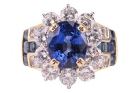 An unheated Burmese sapphire and diamond dress ring, centred with a cushion-cut sapphire of vivid blue colour, approximately 9.6 x 8.0 x 5.6 mm, claw-set within a diamond frame, between shoulders further adorned with diamond accents and 'T' motifs channel
